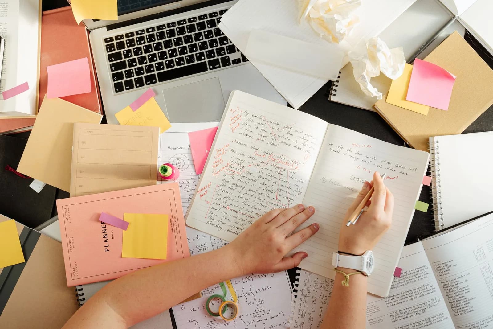 A researcher’s hands organising notes at a desk with a laptop and study materials